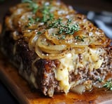 Ein Zwiebelhackbraten auf einem Holzblock, der mit Zwiebeln und Knoblauch garniert ist.